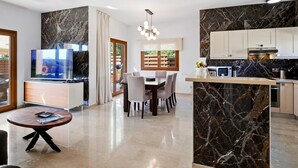 A modern kitchen with marble countertops, a dining area with a table and chairs, and a television in the living area.