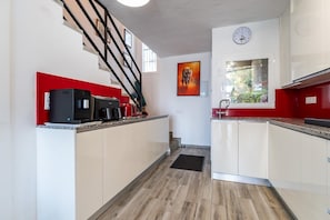 A modern kitchen with white cabinets, a red accent wall, a black coffee machine, and a clock on the wall. - Modern holiday home by beach in Calahonda (Málaga)