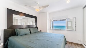 A bedroom with a bed, a ceiling fan, a large mirror, and a window with a view of the sea. - Modern holiday home by beach in Calahonda (Málaga)