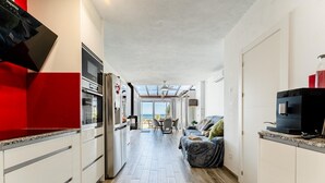 A modern kitchen with white cabinets, a red countertop, and a dining area with a view of the sea. - Modern holiday home by beach in Calahonda (Málaga)