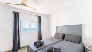 A modern bedroom with a large bed, a ceiling fan, and a view of the sea through a window. - Beachfront holiday home in Malaga (Malaga)