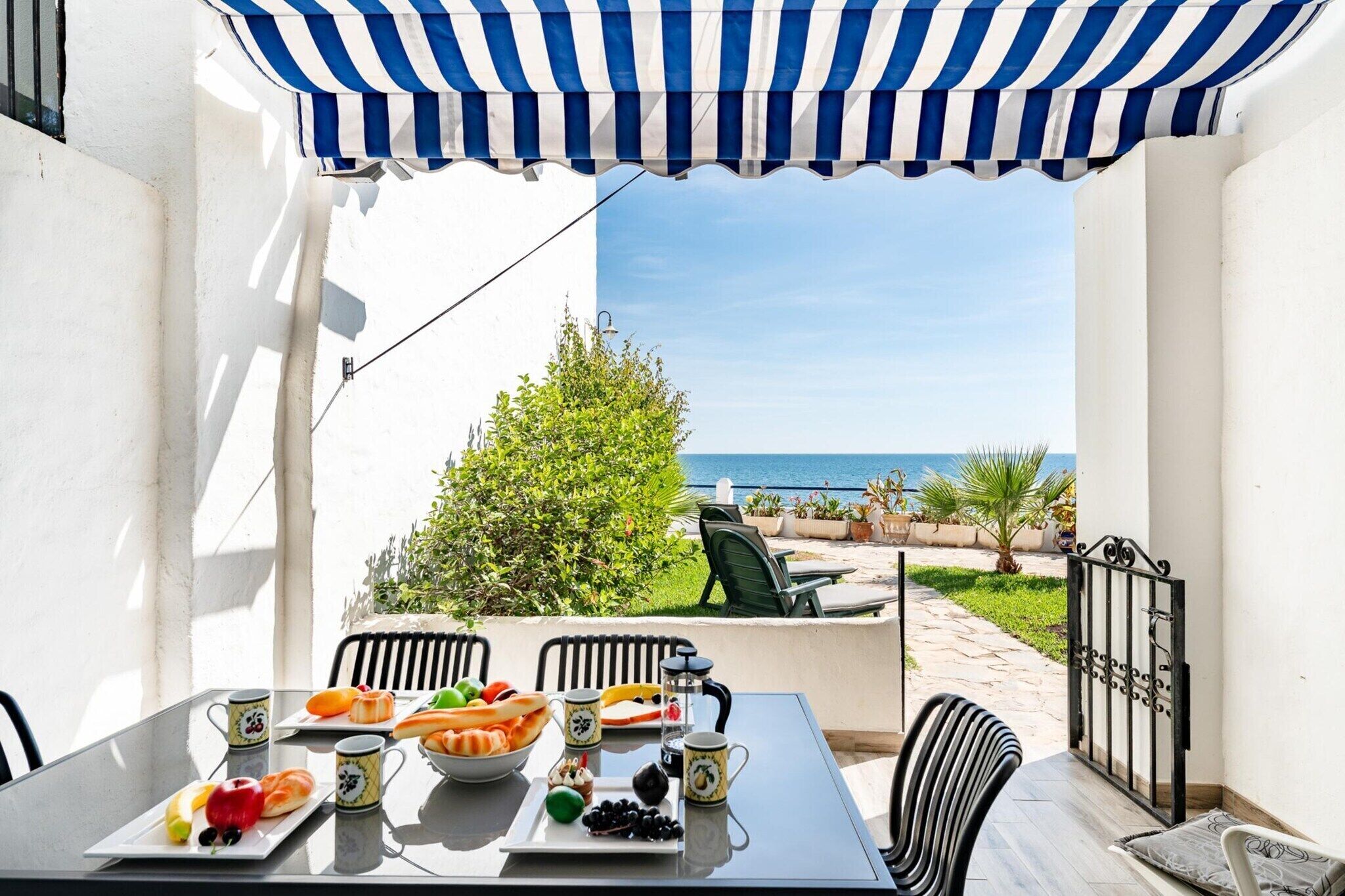 A table set with food and drinks, overlooking a garden and the sea.