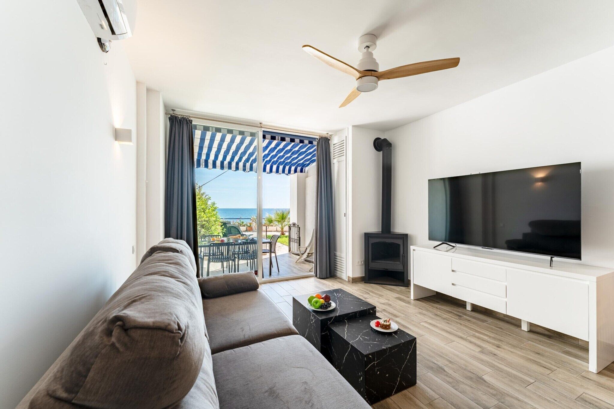 A modern living room with a sofa, a flat-screen TV, a fireplace, and a balcony with a striped awning.