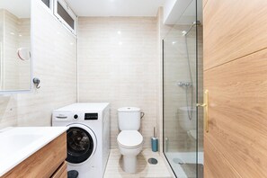 Een moderne badkamer met een douchecabine van glas, een wasmachine en een toilet.