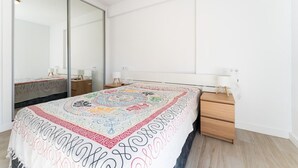 Ein Schlafzimmer mit einem großen Bett, einem Nachttisch aus Holz, einem Spiegel und einer weißen Wand.