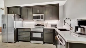 A modern kitchen with dark cabinetry, stainless steel appliances, and a central island with a sink and a coffee machine. - The Goddard 1BR #102-Walking distance to downtown Hot Springs & 6 min to Oaklawn (Hot Springs)