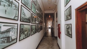 Un couloir orné de nombreuses photographies historiques encadrées, qui mène à une porte au fond.
