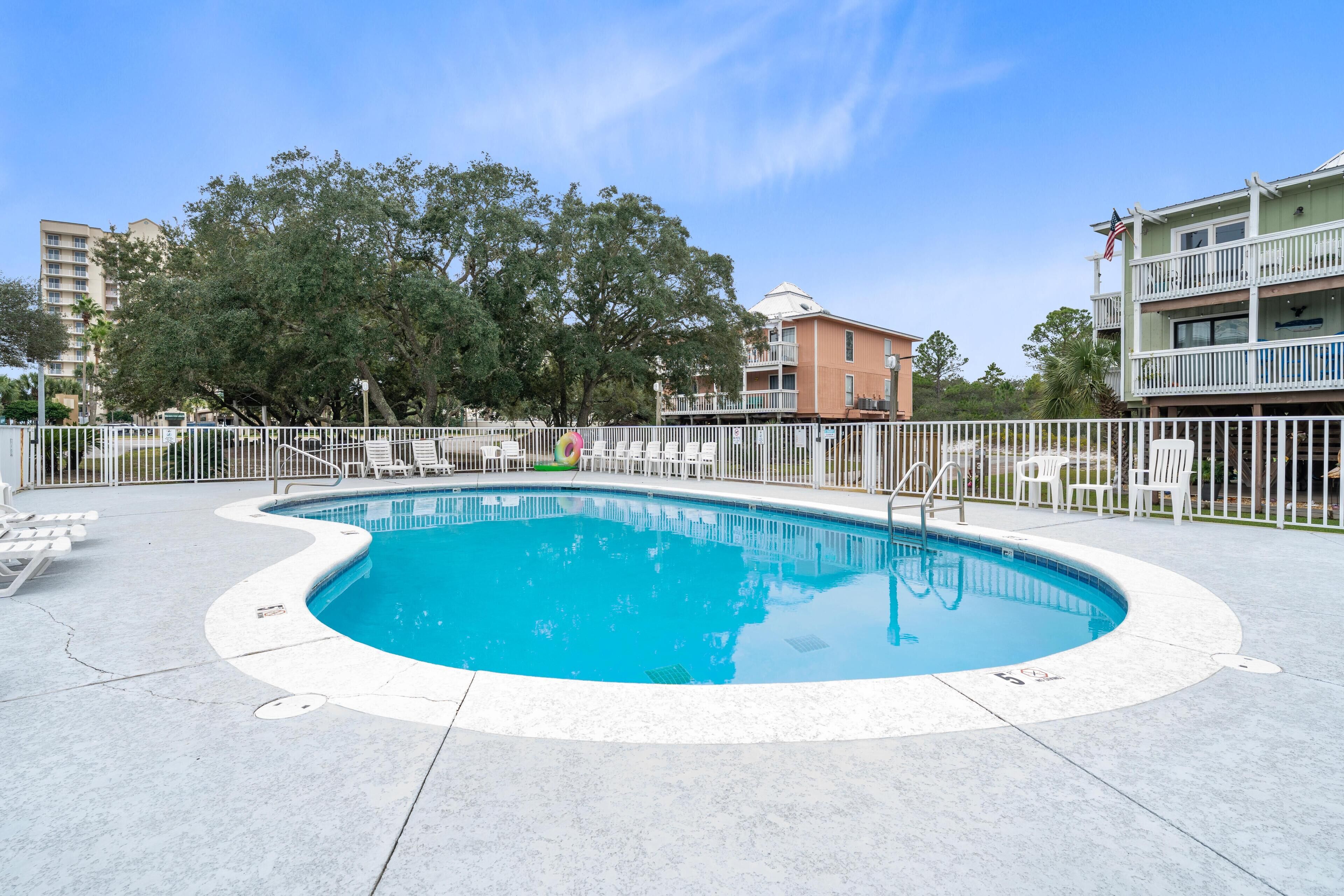 A swimming pool with a curved edge, surrounded by a white fence and lounge chairs.