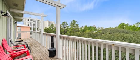 A wooden deck with red chairs and a white railing overlooking a forested area.