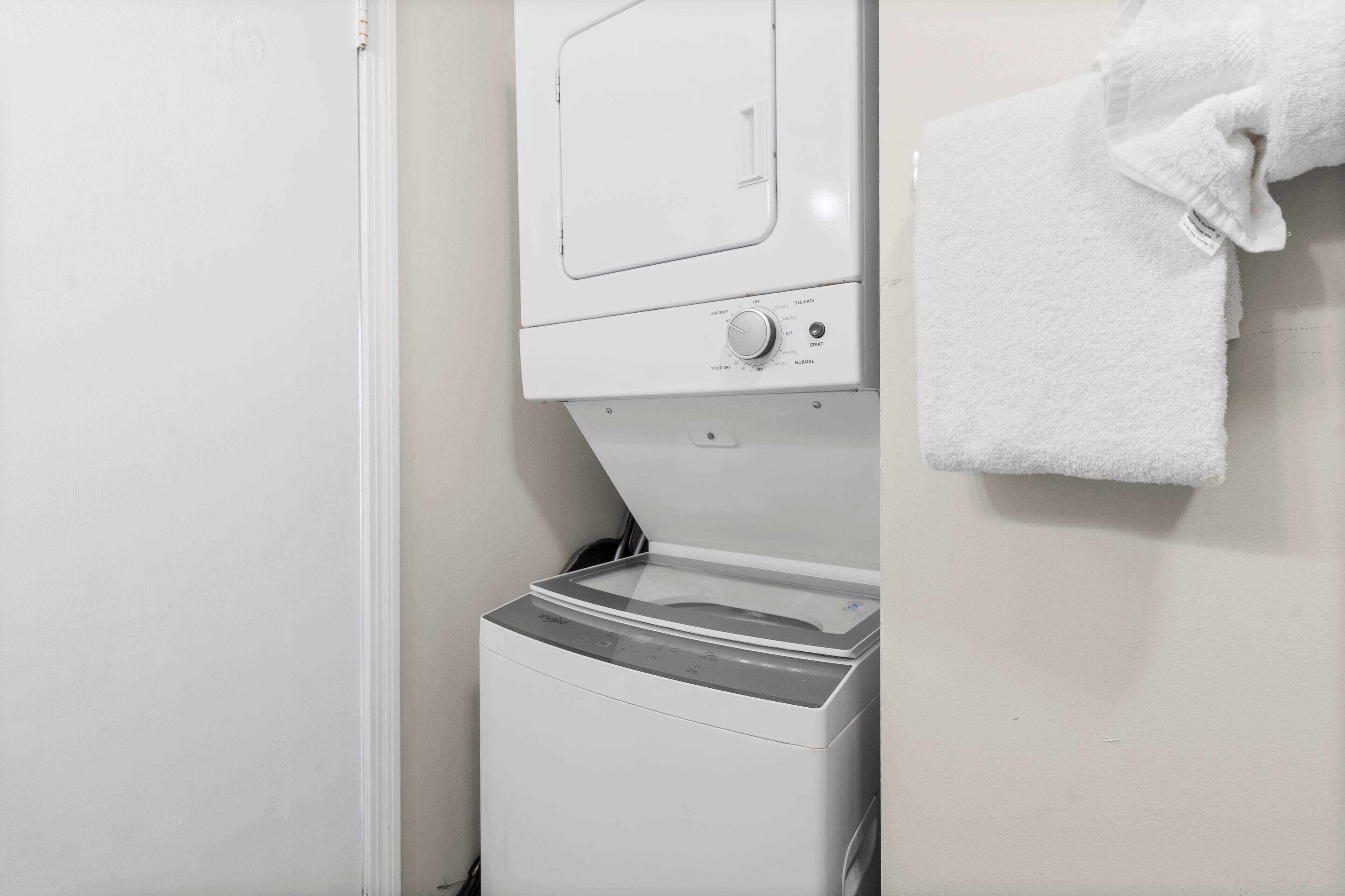 Eine weiße Waschmaschine in einem Badezimmer, ein Handtuch hängt an der Wand.