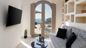 Un salón con sofá, televisor de pantalla plana, una mesa de centro con un libro, una planta en maceta y vista a la playa a través de un ventanal.