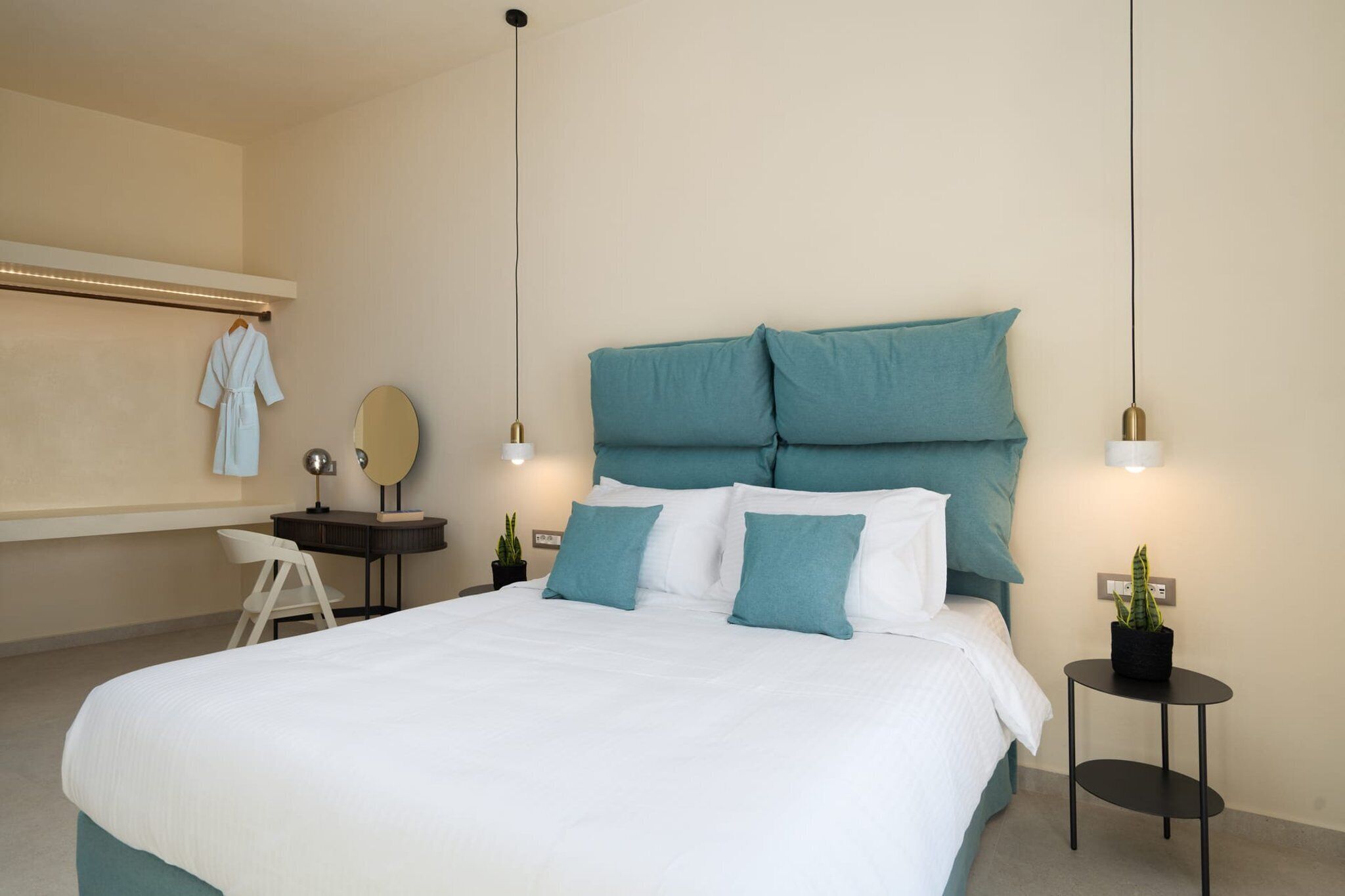 Un dormitorio ordenado con cama, mesitas de noche, escritorio, silla y dos plantas en macetas.