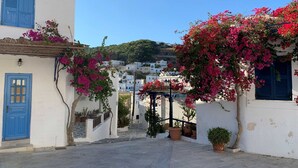 Una calle estrecha con edificios blancos, puertas azules y flores de buganvilla rosadas.