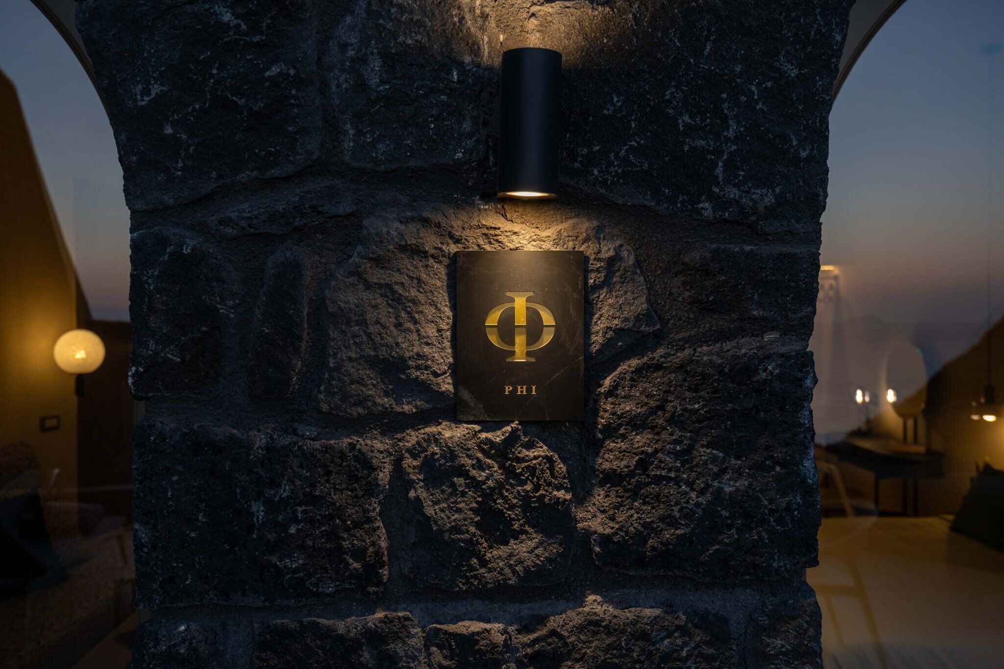 A stone wall with a mounted light fixture and a plaque with the letter 'P' and the word 'PHI'.