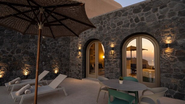 Un edificio de piedra con ventanas de arco, asientos exteriores y una mesa con sillas.