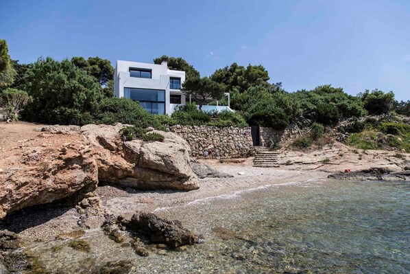 Una casa moderna con un muro de piedra y una vista despejada del mar.