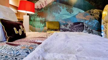 Een bed met een beddekleed met een patroon, een kussen met de tekst 'LOVE', een rode lamp en een groene stoel.