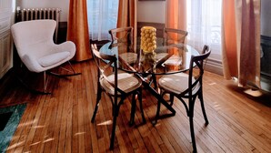 Una habitación con una mesa redonda de vidrio, cuatro sillas, un sillón blanco, un radiador y un cuadro en la pared.