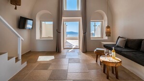 Une pièce spacieuse avec vue sur la mer, un escalier, un téléviseur à écran plat et un coin salon confortable avec une bouteille et des verres.