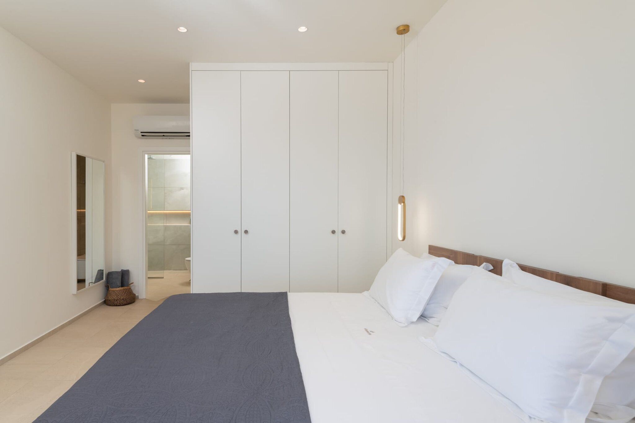 A bedroom with a bed, white walls, a wardrobe, and an air conditioning unit.