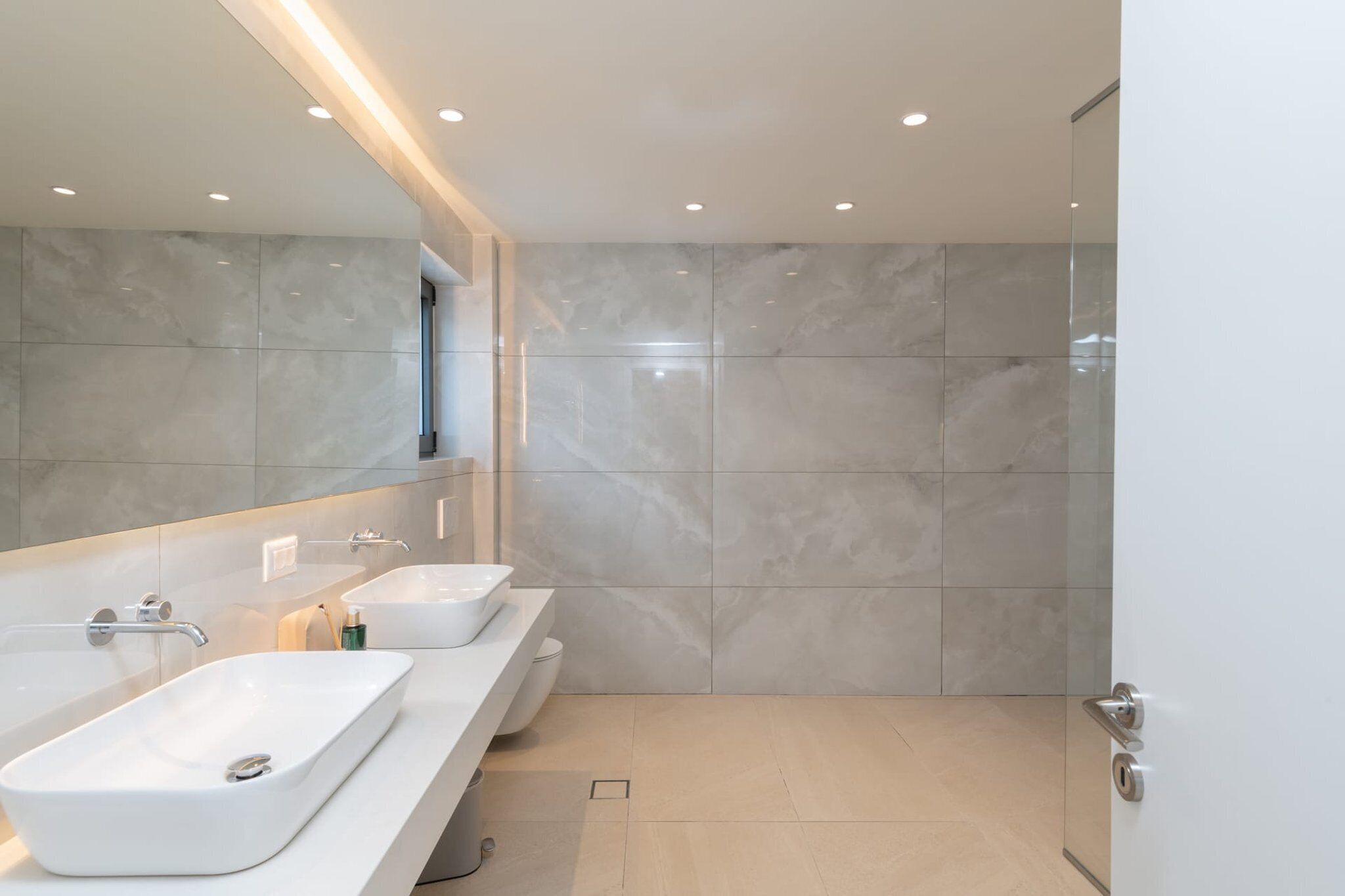 Un baño moderno con un espejo grande, dos lavamanos y una zona de ducha.