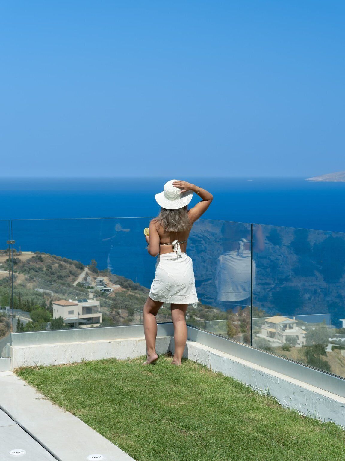 Una persona de pie en un balcón con vistas a un paisaje costero y una vista despejada del mar y la costa distante.