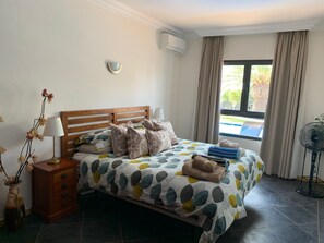 A neatly made bed with a leaf-patterned bedspread, a wooden bedside table with a lamp, and a vase with dried flowers. - Villa Marisma | 3 Bedrooms | Private Pool | Prime Location | Furnished Terrace. (Playa Blanca)