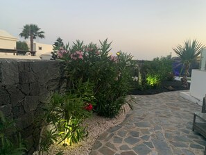 A stone pathway leading to a building, surrounded by greenery and a stone wall. - Villa Marisma | 3 Bedrooms | Private Pool | Prime Location | Furnished Terrace. (Playa Blanca)