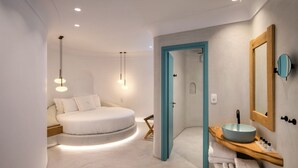 Un dormitorio moderno con una cama redonda, un tocador de madera con un lavabo grande y un espejo.