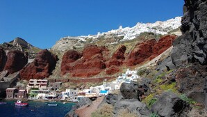 Un pueblo costero con edificios blancos, acantilados rocosos y barcos en el puerto.