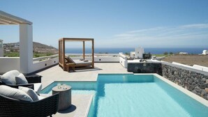 A rooftop pool area with a clear view of the ocean, a wooden lounge chair, and a stone wall. - Alluring Santorini Villa | Eruption Escape Villa | Villa with Private Pool &. (Santorini)