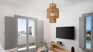 A modern living room with a flat-screen TV, a wooden coffee table, and a large window overlooking a pool. - Alluring Santorini Villa | Eruption Escape Villa | Villa with Private Pool &. (Santorini)