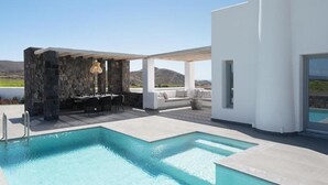 Un área de piscina moderna al aire libre con una estructura de piedra, asientos y vistas al paisaje.
