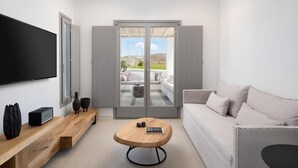 Una sala de estar moderna con un televisor de pantalla plana, una mesa de centro de madera, un sofá y un patio de cristal corredizo que da a una zona de estar exterior.