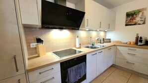 Een moderne keuken met witte kasten, een zwarte afzuigkap, een ingebouwde oven, een vaatwasser en een spoelbak met een kraan.