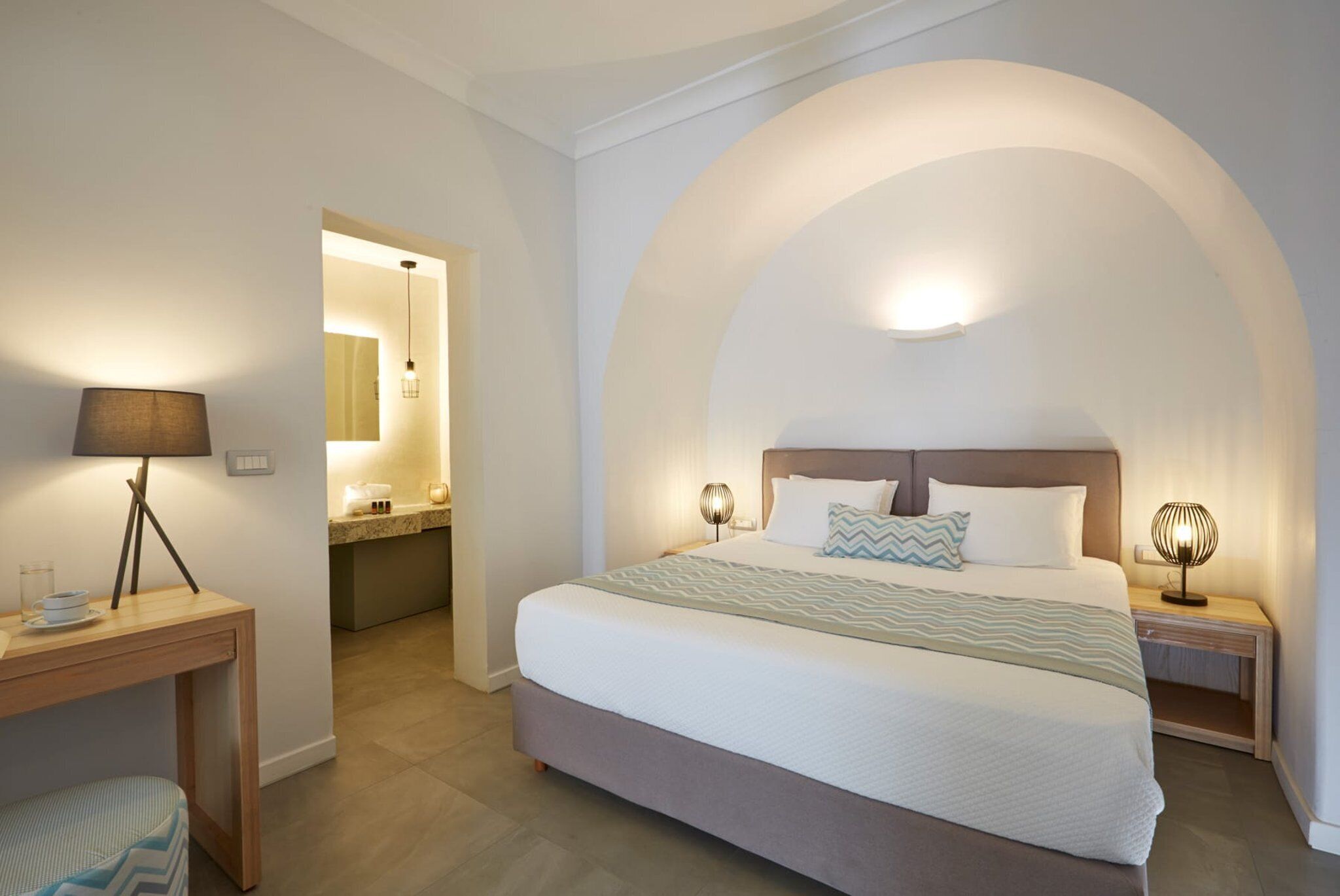 A bedroom with a large bed, bedside lamps, a desk, and a chair.