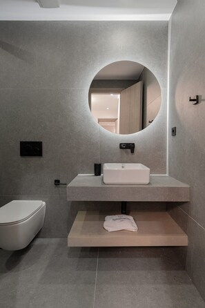 Een moderne badkamer met een ronde spiegel, een witte wastafel en een toilet.