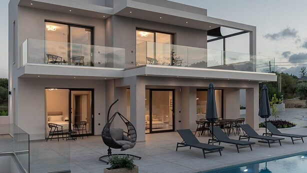 Een modern huis met twee verdiepingen, een zwembad, buitenzitplaatsen en een glazen balustrade.