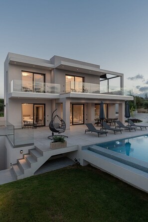Een modern huis met twee verdiepingen, een zwembad, buitenzitplaatsen en een glazen balustrade.