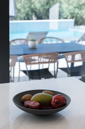 Een schaal met fruit op een tafel, met uitzicht op een zwembad en terrasjes op de achtergrond.