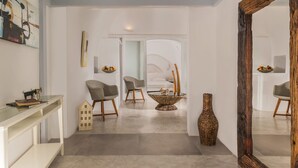 Ein modernes Wohnzimmer mit einem Glastisch, zwei Sesseln, einem Holznachttisch und einem großen Spiegel.