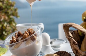 A clear glass bowl filled with cereal and milk, with a spoon pouring more milk. - Endearing Santorini Suite | Selene Moonlight Cave Suite | Breathtaking Caldera. (Oia)