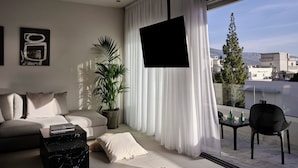 Uma sala de estar moderna com sofá, mesa de centro, TV e varanda com vista para edifícios e árvores.