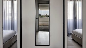 Quarto de hotel moderno com design minimalista, apresentando uma grande porta deslizante que dá para uma varanda com vista para a cidade.