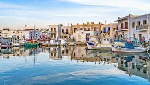 Un puerto con barcos amarrados, edificios con balcones y una superficie de agua tranquila que refleja las construcciones.