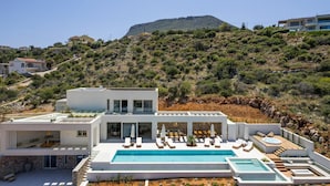 A modern villa with a swimming pool, outdoor seating, and a view of a hill. - Elegant Crete Villa | Villa Cretan Soul | 5 Bedrooms | Prviate Pool |. (Crete)