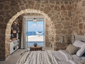 A bedroom with a stone wall, a hammock by the window, and a view of the sea. - Villa Aegean Horizon | Vasilikos | 4 En-suite Bedrooms | Infinity Pool |. (Zakynthos)