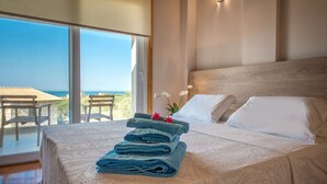 Une chambre avec une grande fenêtre, un lit recouvert de draps blancs et une vue sur la mer.