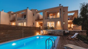 Une maison moderne à deux étages, dotée d’une piscine, d’un espace salon extérieur et d’un mur en pierre.