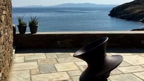 Eine Steinterrasse mit einem schwarzen Stuhl, Blumentöpfen und Blick auf das Meer und die entfernten Berge.